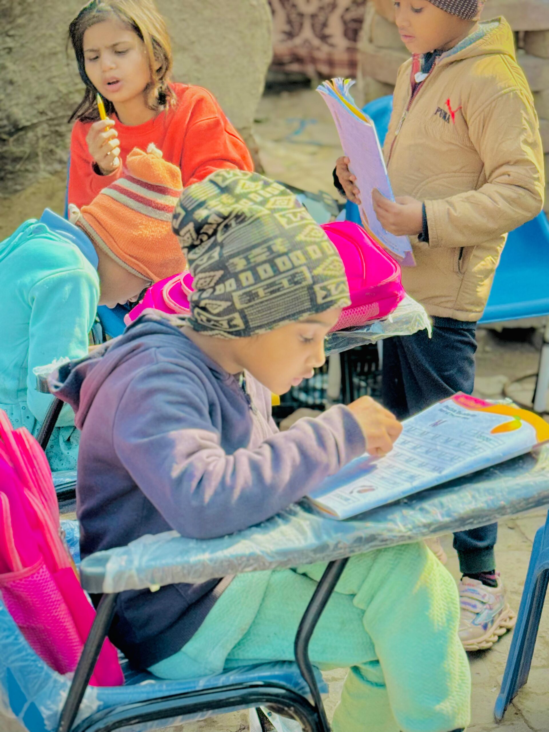 Child writing in a workbook during outdoor education support in Pakistan